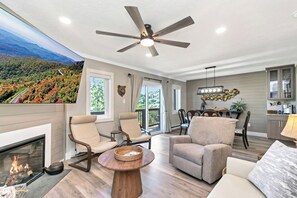 A spacious living room with a fireplace, comfortable seating, a dining area, and a view of a forested landscape. - The Only True Ski-in/ski-out Resort @ Sugar Mtn (Sugar Mountain)