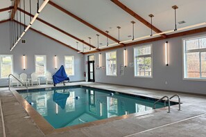 Ein Hallenbad mit freiem Blick auf die Decke, Holzbalken und einer Sitzgruppe mit Stühlen.