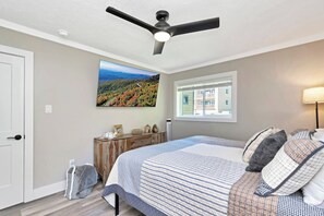 A bedroom with a bed, a ceiling fan, a window with blinds, a wall-mounted TV, and a bedside table with decorative items. - The Only True Ski-in/ski-out Resort @ Sugar Mtn (Sugar Mountain)
