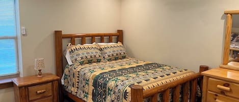 Un dormitorio con cama de madera, mesita de noche, cómoda, ventilador de techo y ventana con persianas.