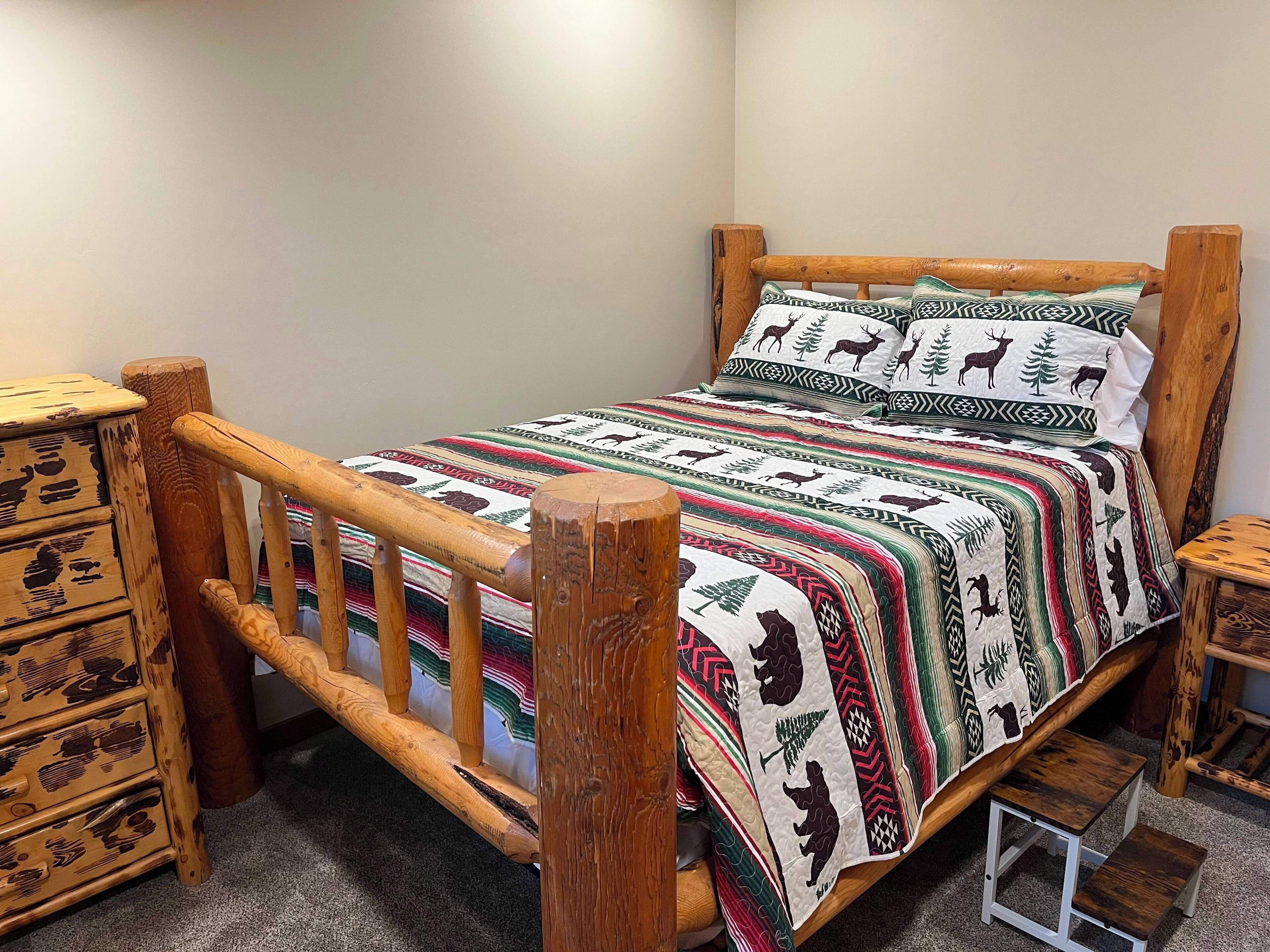 A wooden bed with a patterned bedspread and matching pillows, flanked by wooden nightstands and a dresser.