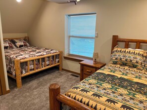 A bedroom with two wooden beds, a window with blinds, a bedside table with a lamp, and a carpeted floor. - NEW Bear Lake Cabin in Garden City (Garden City)