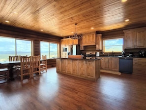 A spacious kitchen with wooden cabinets, a central island, and large windows offering a view of the outdoors. - NEW Bear Lake Cabin in Garden City (Garden City)