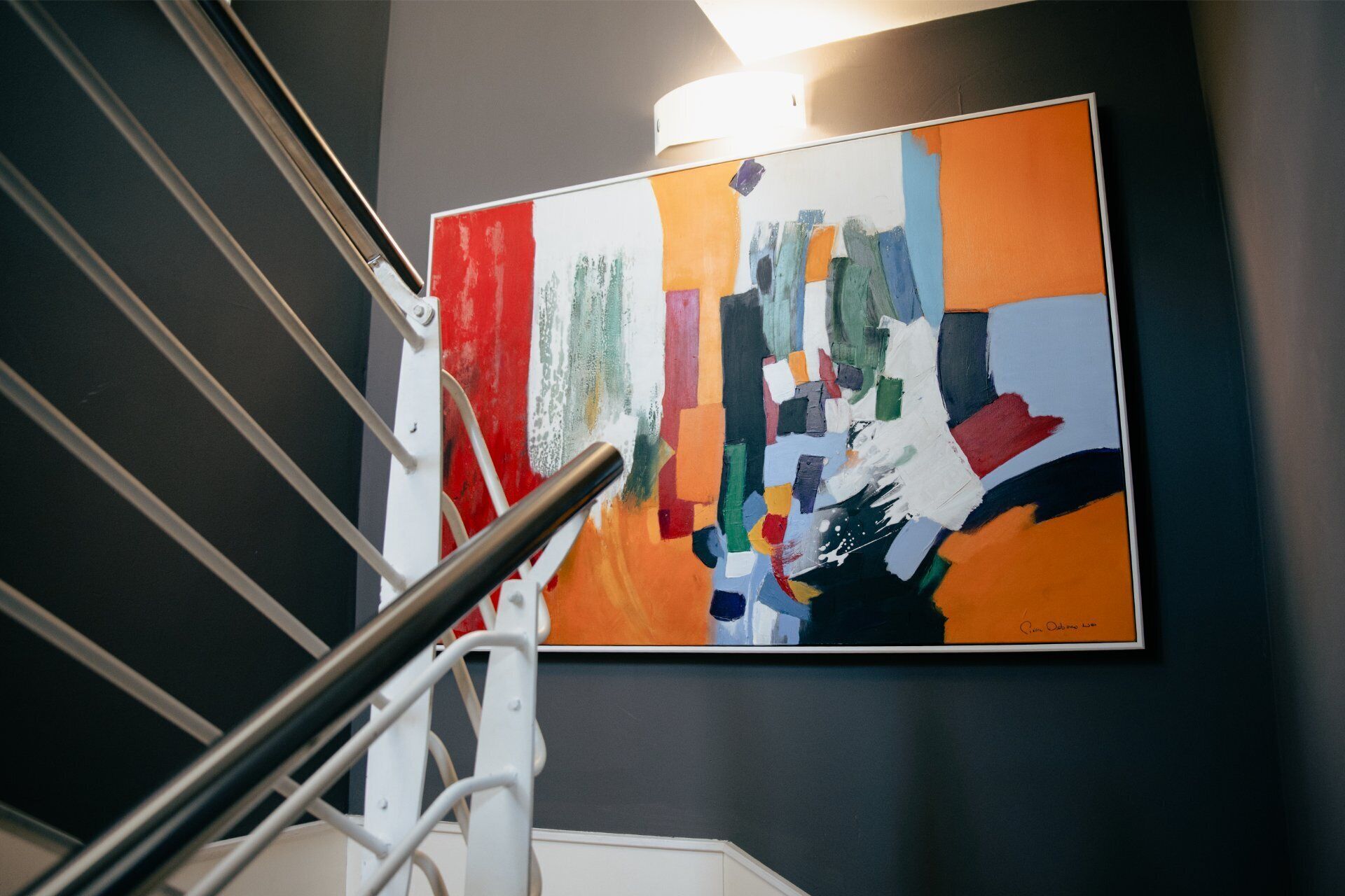 A staircase with a handrail leading to a room with a large abstract painting on the wall.