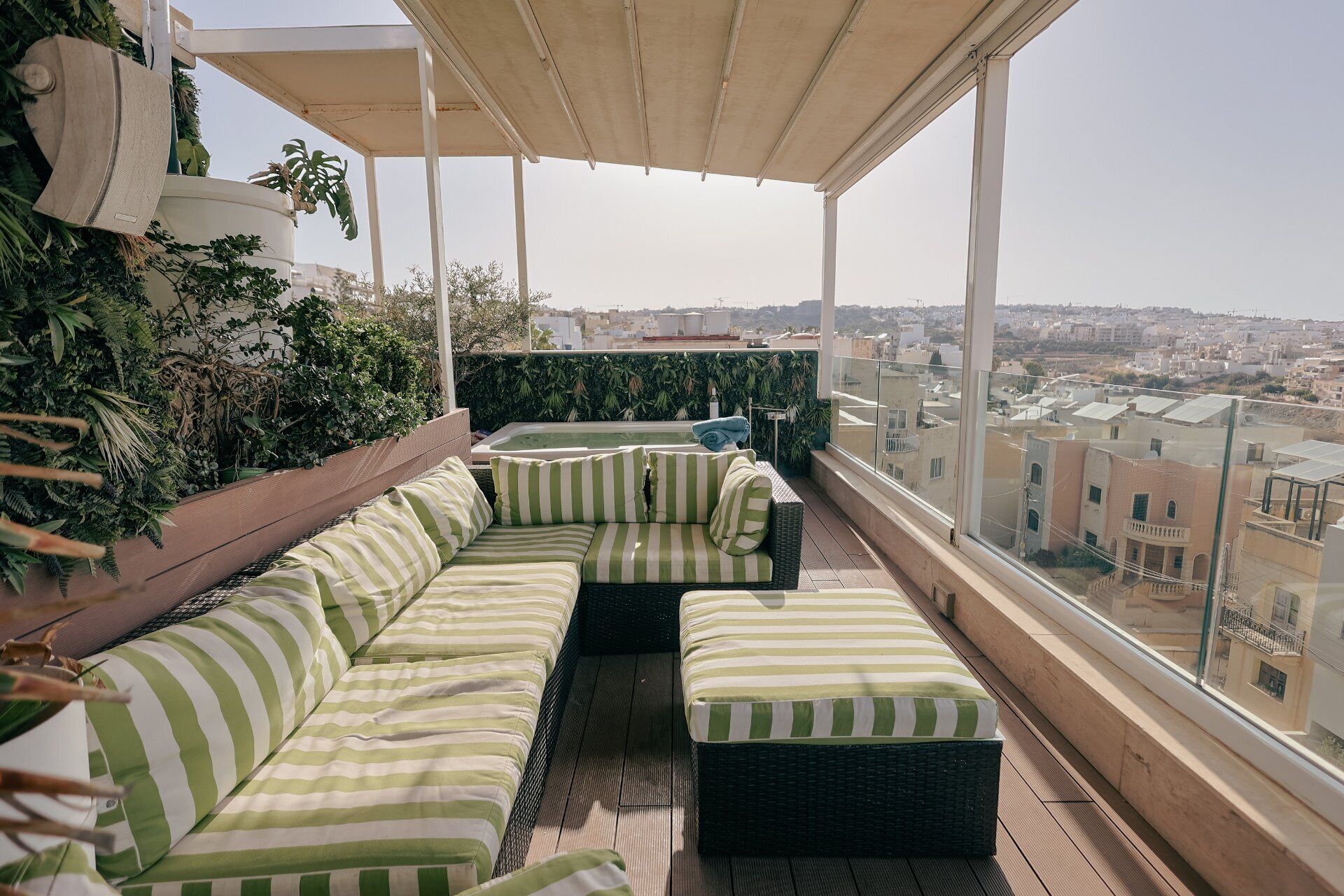 Una terraza en la azotea con un conjunto de sofá a rayas verdes, una mesa pequeña y una bañera de hidromasaje.