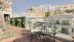 En takterrass med ett metallbord och stolar, krukväxter och utsikt över de omgivande byggnaderna.