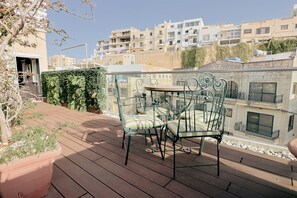A rooftop terrace with a metal table and chairs, potted plants, and a view of surrounding buildings. - Luxury Duplex With Jacuzzi, Stunning Views (St. Julian's)
