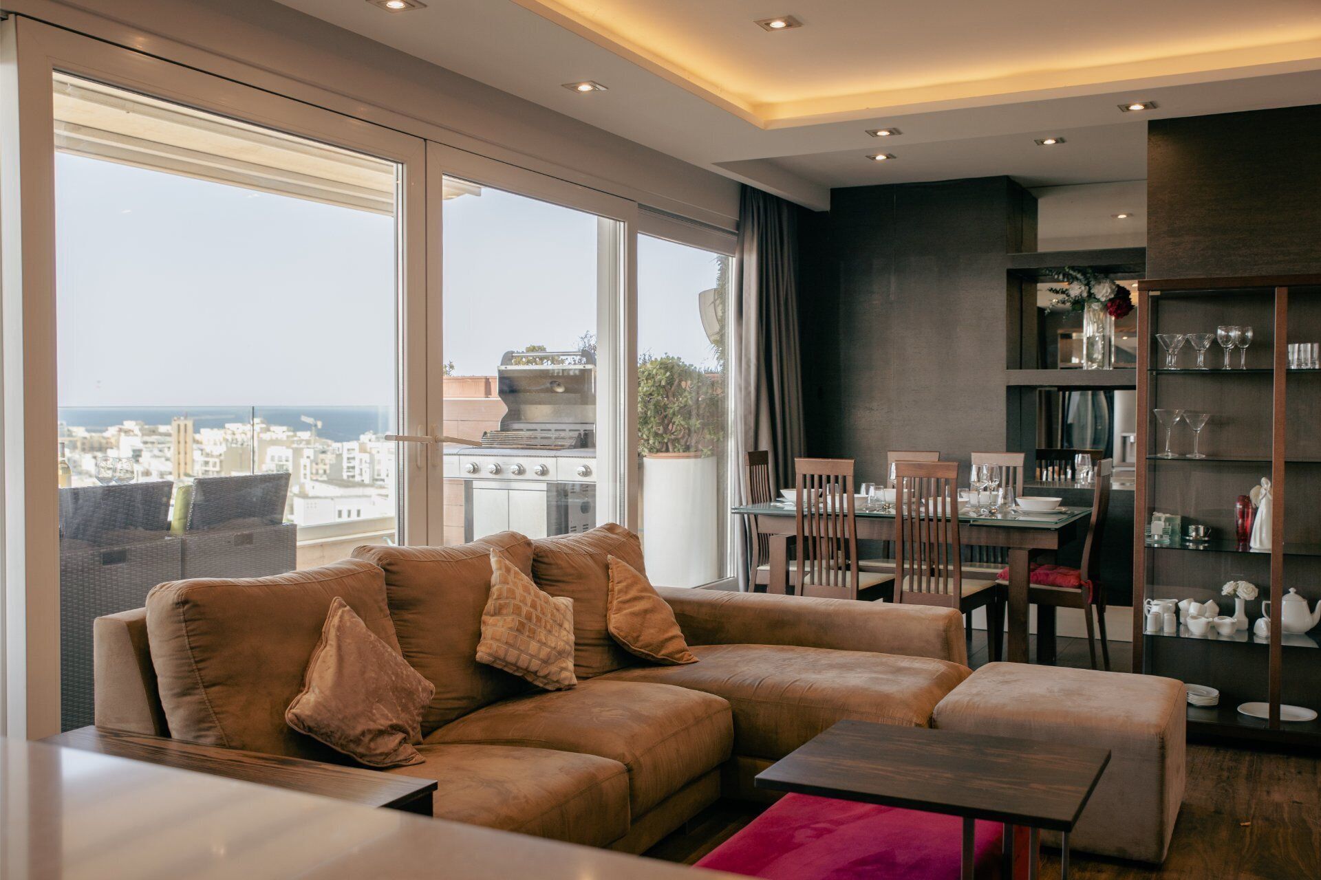 A modern living room with a large window, a sofa, a dining table, and a bookshelf.