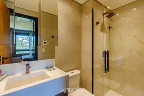 Ein modernes Badezimmer mit Duschabtrennung aus Glas, einem weißen Waschbecken mit zeitgemäßer Armatur und einer Toilette.