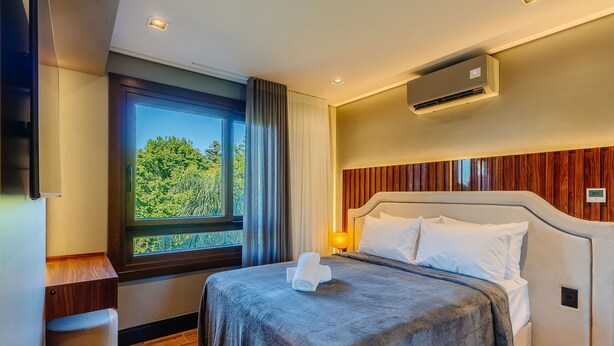 A modern hotel room with a large bed, a nightstand, a window with curtains, and an air conditioning unit. - Beautiful Apartment in Gramado Dms0304 (Gramado)