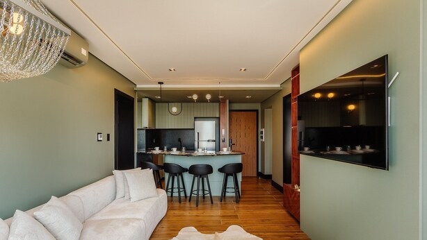 A modern living room with a sofa, a dining area with stools, a kitchen with a bar, and a mounted TV. - Exclusivity in the Heart of Gramado! Dms0203 (Gramado)
