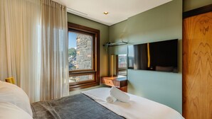 A hotel room with a bed, a television, a stone wall, and a window with curtains. - Exclusivity in the Heart of Gramado! Dms0203 (Gramado)