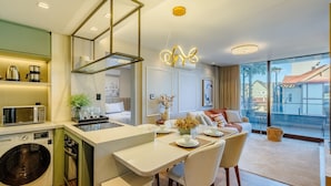 A modern hotel room with a kitchen, dining area, and a large window offering a view of the outside. - Apt w/ Balcony, Fireplace & View in Center Dms0107 (Gramado)