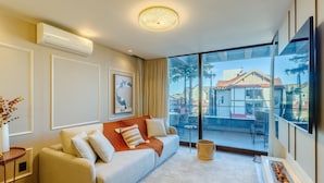 A modern living room with a sofa, a coffee table, a large window with a view of the outside, and a ceiling light fixture. - Apt w/ Balcony, Fireplace & View in Center Dms0107 (Gramado)