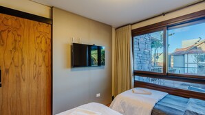 A hotel room with a bed, a TV mounted on the wall, and a window with a view of buildings outside. - Apt w/ Balcony, Fireplace & View in Center Dms0107 (Gramado)