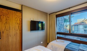 Ein Hotelzimmer mit Bett, Wandfernseher und Fenster mit Blick auf Gebäude.