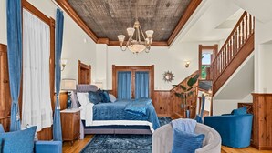 A spacious bedroom with a large bed, wooden ceiling, and a staircase.