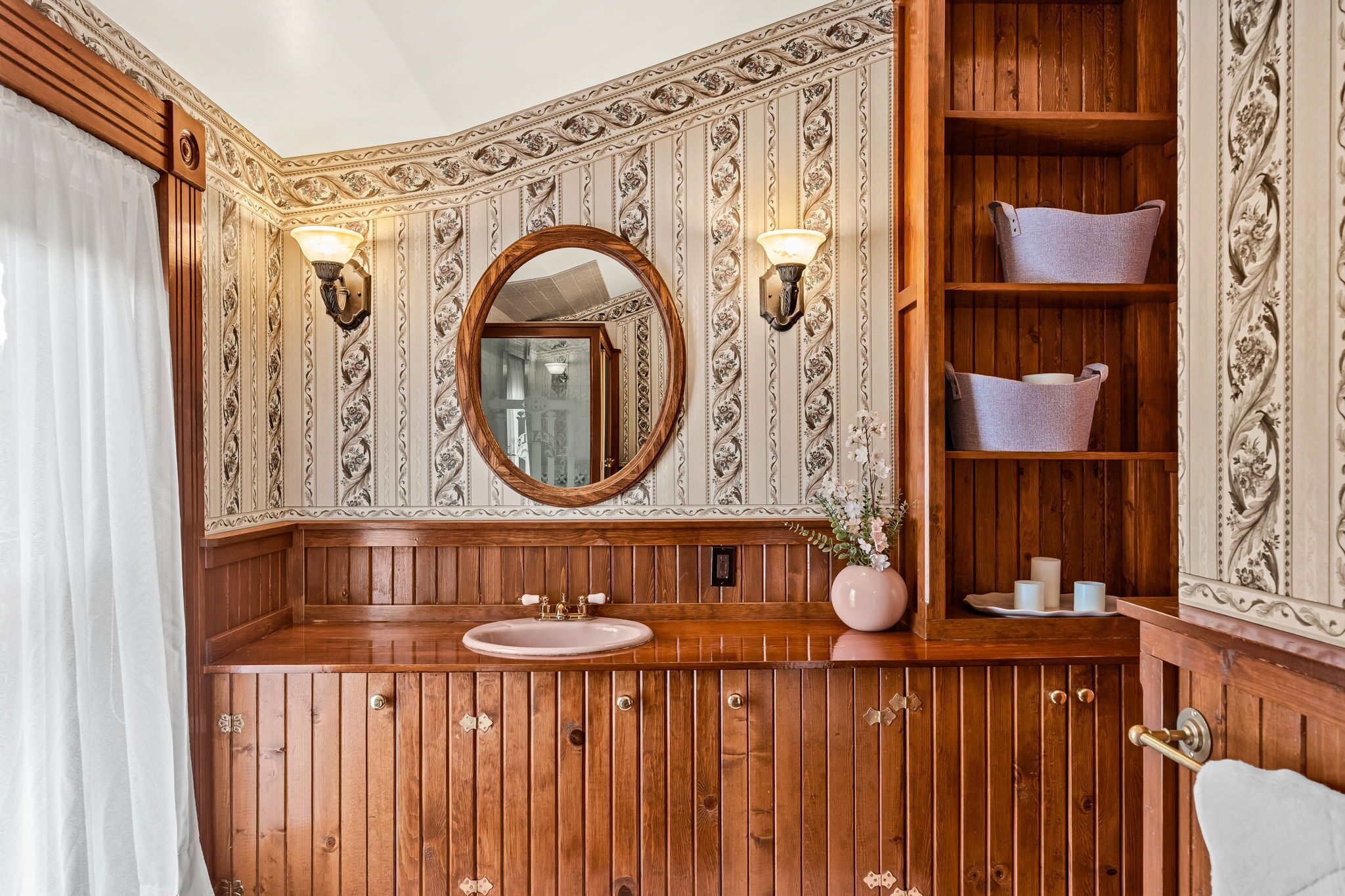 A wooden vanity with a round mirror, a sink, and two wall sconces.