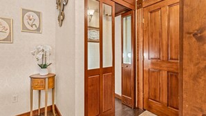 A wooden door with a glass panel, a small wooden side table with a plant, and a wall with framed artwork.