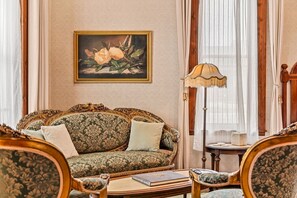 A room with a patterned sofa, a side table with a lamp, and a framed painting on the wall.