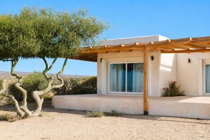 Ein modernes Haus mit einer Pergola, großen Fenstern und einer Wüstenlandschaft.