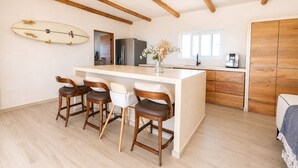Eine moderne Küche mit einer zentralen Kochinsel, Holzbarhocker, einem Surfbrett an der Wand und einem Kühlschrank.