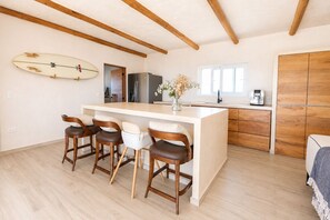 Eine moderne Küche mit einer zentralen Kochinsel, Holzbarhocker, einem Surfbrett an der Wand und einem Kühlschrank.