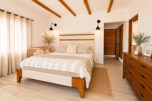 Une chambre à coucher comprenant un lit, des lampes de chevet, une table de chevet, une commode et une porte donnant sur une autre pièce.