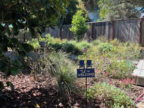 Uma área de jardim com placa de boas-vindas, cerca de madeira e diversas plantas.