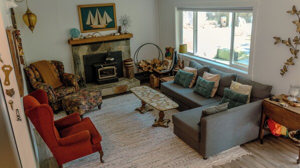 A cozy living room with a fireplace, a sofa, a red armchair, and a large window providing a view of the outdoors.