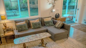 A living room with a sectional sofa, a coffee table, and a red armchair. There is a window with a view of the backyard.