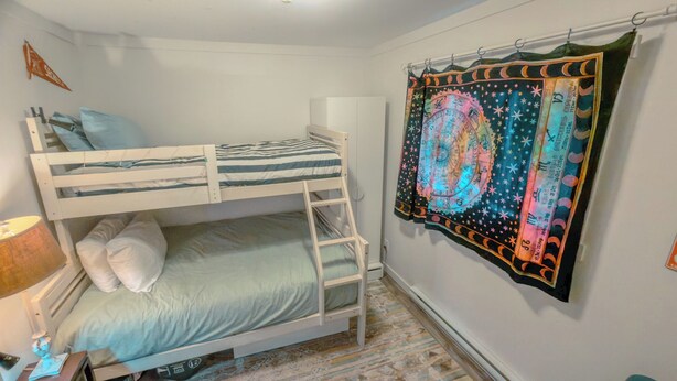 A bunk bed room with a ladder, a wall-mounted tapestry, and a lamp.