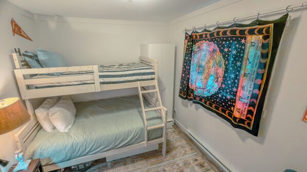 A bunk bed room with a ladder, a wall-mounted tapestry, and a lamp.