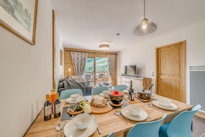 A dining area with a wooden table set for a meal, a television in the background, and a view of the outdoors. - 50m from ski slopes, 2nd floor, balcony, parking, tv, ski locker, 64m², Champagny-en-Vanoise (Champagny-en-Vanoise)