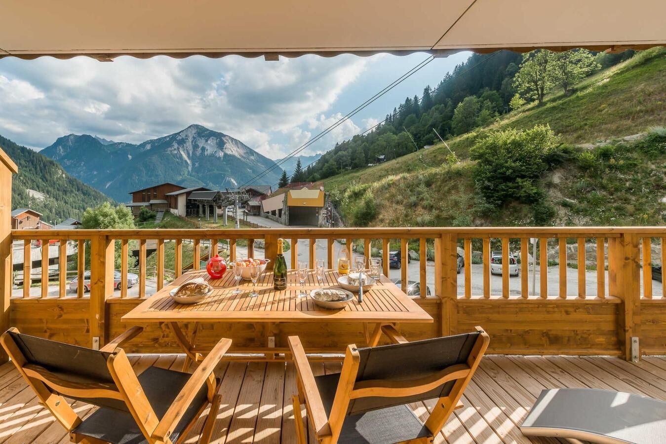 Una terraza de madera con una mesa dispuesta para comer, con vistas a un paisaje montañoso.