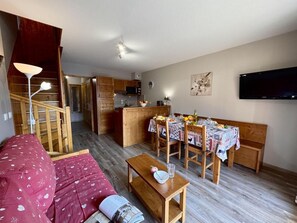 A cozy living room with a sofa, a wooden dining table set for four, and a kitchen area with wooden cabinets and a flat-screen TV. - 50m from ski slopes, 4th floor, swimming pool, balcony, ski locker, 50m², Vars (Vars)