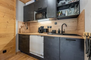 A modern kitchen with dark cabinets, a built-in microwave, a sink, and a coffee machine. - 200m from ski slopes, 1st floor, swimming pool, balcony, tv, ski locker, 30m², Les Orres (Les Orres)