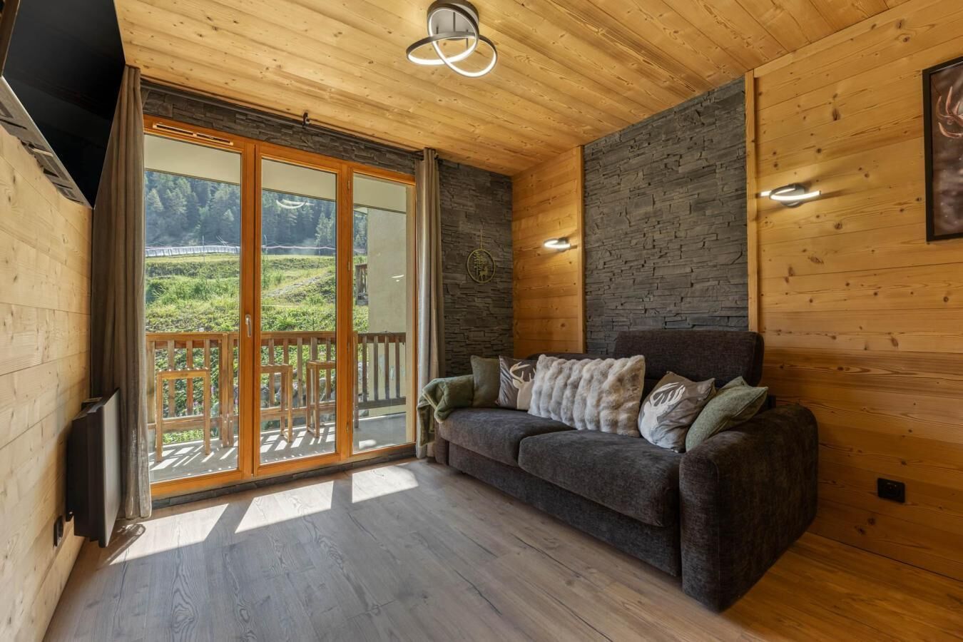 A wooden interior with a sofa, a stone wall, and a view through a glass door.