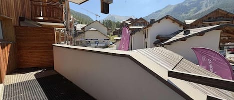 Un balcon donnant sur une chaîne de montagnes, avec des balustrades en bois et un bâtiment à la façade blanche.