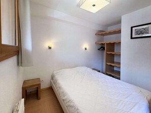 Een slaapkamer met een bed, nachtkastjes, een wandplank en een plafondlamp.