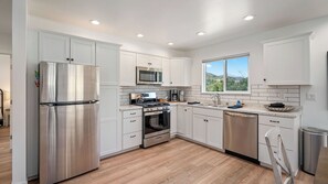 A modern kitchen with stainless steel appliances, white cabinetry, and a window with a view. - Stampede Loft at The 8 Mile by Avantstay Private Porch + Full Kitchen Ranch Acreage + Trails (Santa Margarita)
