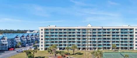 A hotel with multiple floors, outdoor swimming pools, and a tennis court.