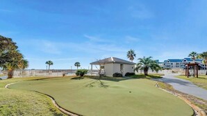 A golf course with a clubhouse, palm trees, and a clear sky. - Beachfront Getaway w/ Pools, Sauna & Ocean Views (Gulf Shores)