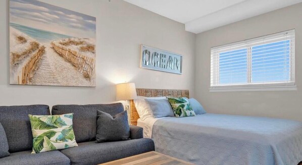Ein Schlafzimmer mit Bett, Schlafsofa, Nachttisch, Lampe und einem Bild mit Strandmotiv.