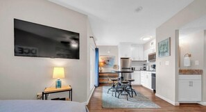A modern kitchen with white cabinets, a dining area with a table and chairs, and a TV mounted on the wall. - Beachfront Getaway w/ Pools, Sauna & Ocean Views (Gulf Shores)