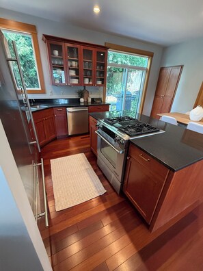 A kitchen with wooden cabinets, a stainless steel refrigerator, a gas stove, and a built-in oven. - Charming Indianola home, Walk to Beach, & Pier (Indianola)
