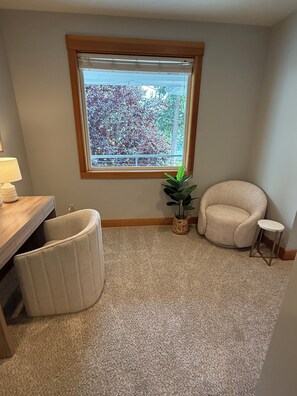 Ein Eckzimmer mit Fenster, einem Sessel, einem kleinen Tisch und einem Blumentopf.
