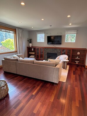 Ein Wohnzimmer mit einem großen, beige gefärbten Sofa, einem Kamin, einem Flachbildfernseher und Holzböden.