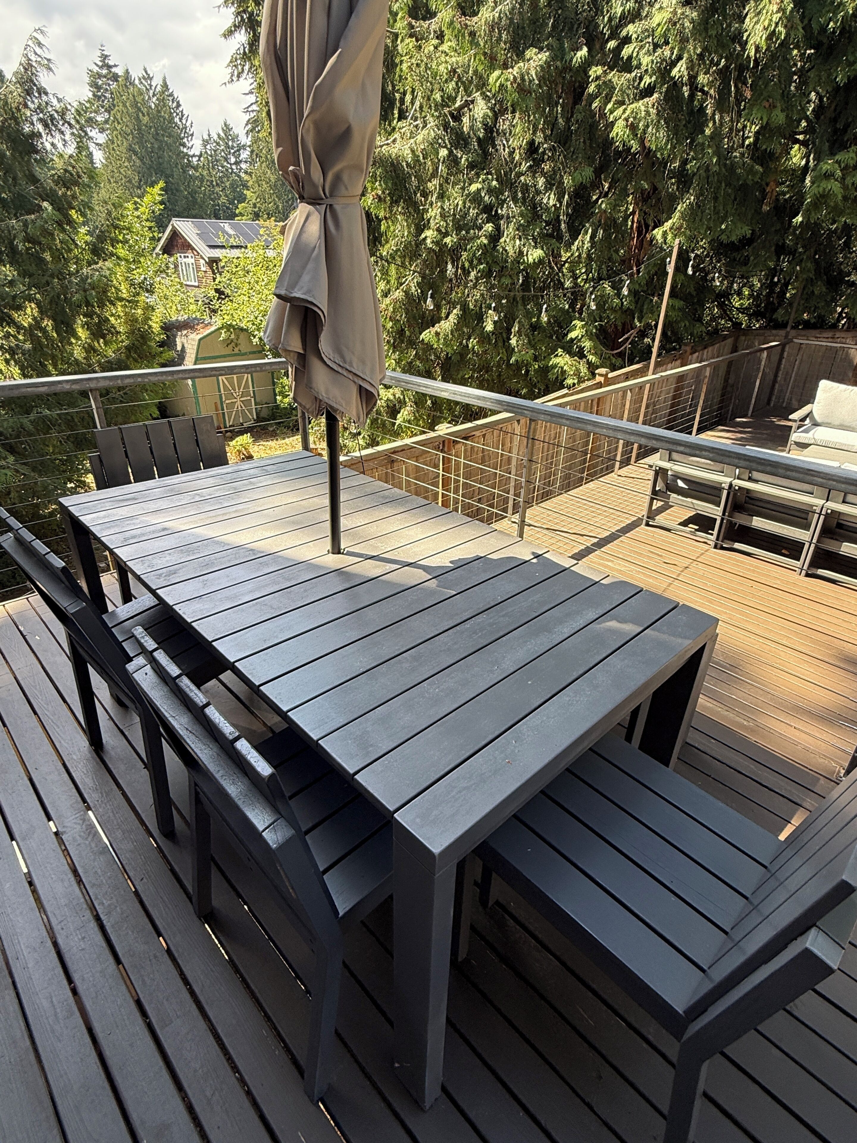 Eine Terrasse mit Tisch und Stühlen, umgeben von einem Holgitter und Blick auf Bäume.