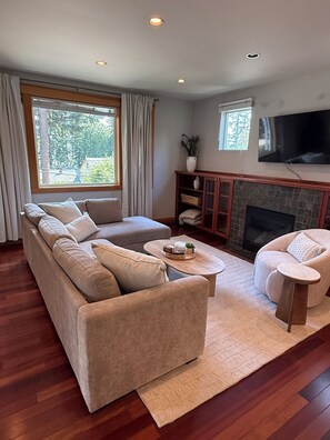 A living room with a sectional sofa, a coffee table, a fireplace, and a television mounted on the wall. - Charming Indianola home, Walk to Beach, & Pier (Indianola)